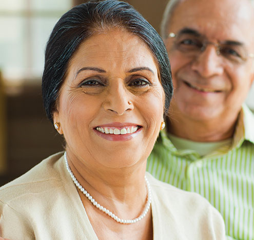 A woman smiling with a man behind her. Links to What to Give